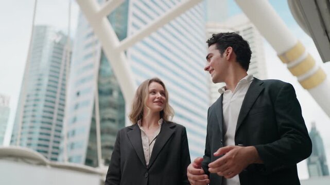 Businesspeople walk near modern buildings. They appear engaged, smiling, and conversing. Urban setting suggests a professional meeting or discussion