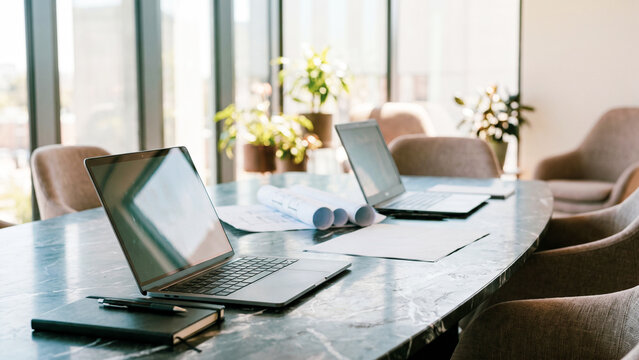 Modern office conference table with open laptop, architectural blueprints and notebook, professional business workspace
