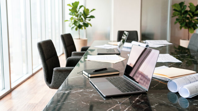Modern office conference table with open laptop, architectural blueprints and notebook, professional business workspace