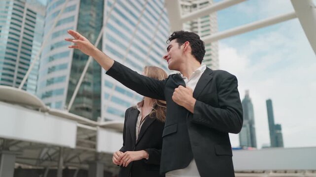 Young professionals walk through modern cityscape. They gesture toward skyscrapers, sharing ideas. Businesspeople appear focused, confident