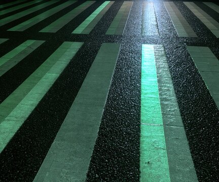 Retro-reflective tape strips on wet asphalt illuminated by a hard torch beam, creating a dark and ordered pattern for road safety backgrounds