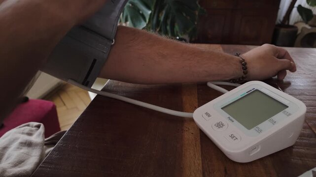 Close-up shows a male patient wearing an arm cuff while checking blood pressure on a digital home diagnostic device, illustrating routine healthcare monitoring.