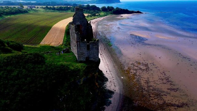 FPV drone flight around Greenan Castle at Ayr, Scotland, revealing the historic coastal ruin above a sandy beach, farmland and the Firth of Clyde