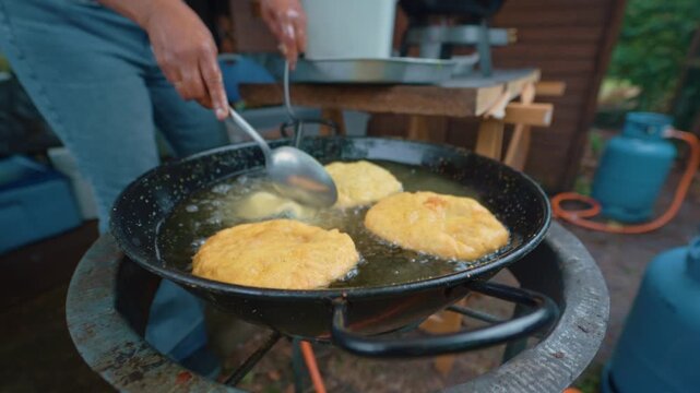 Close up of woman adding Bara dough to the frying pan lit by propane gas at an outdoor event. surinamese street food. cultural dish.