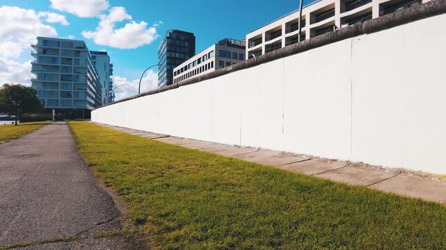 walking along white wall at Berliner wall concrete barrier on a sunny afternoon.