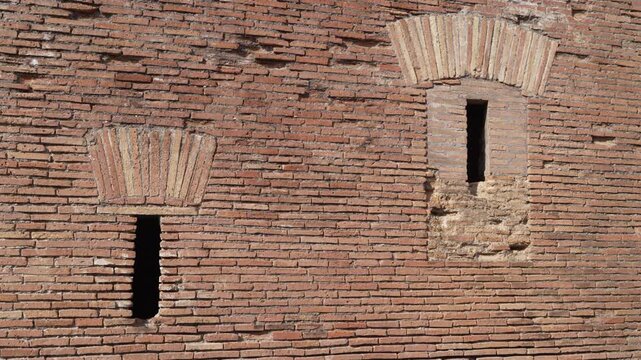 Two narrow slit windows punctuate a flat Roman masonry wall, revealing brick texture and construction details.