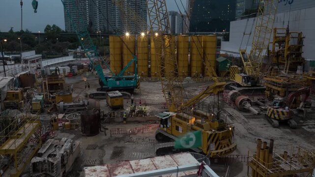 Night timelapse of active urban construction site with illuminated yellow silos and heavy excavators