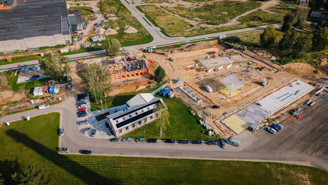 Aerial view of a construction site with multiple buildings under development, surrounded by vehicles, green grass, and a road, showcasing ongoing urban development in a suburban area