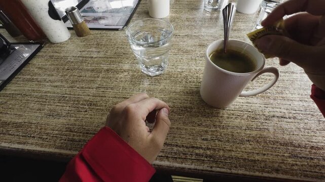 A comforting, cozy first-person view of a traveler resting at a diner table. mindfully adding brown sugar to a cup , enjoying a completely calm, peaceful moment of solitude to warm right up alone