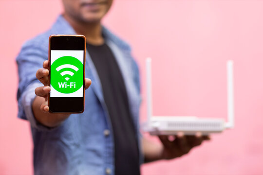 Person Holding Smartphone Displaying Wi-Fi Symbol with Wireless Router
