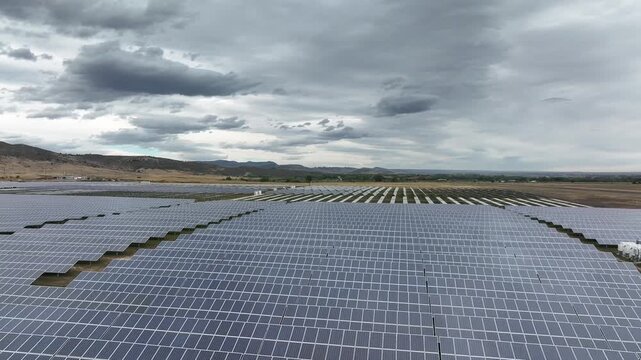 A vast Colorado solar farm tracks moody, overcast skies. This cinematic look at green tech captures daylight harvesting panels under low grey clouds, pushing forward the renewable energy transition.