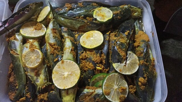 Traditional Indonesian seasoned catfish topped with lime slices, served in a container at a local street food bazaar, authentic culinary background.