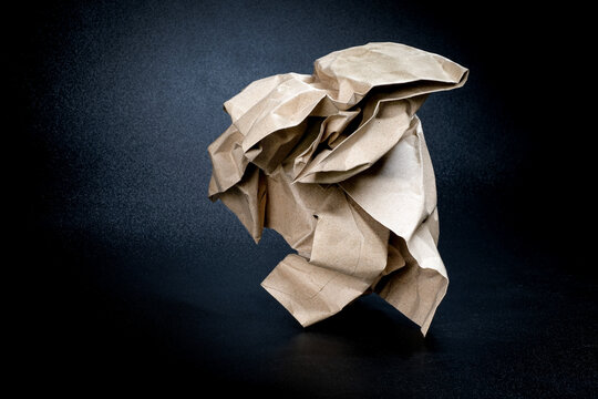 Close-up of a crumpled brown kraft paper ball resting on a dark surface under dramatic spotlight symbolizing a rejected creative idea.