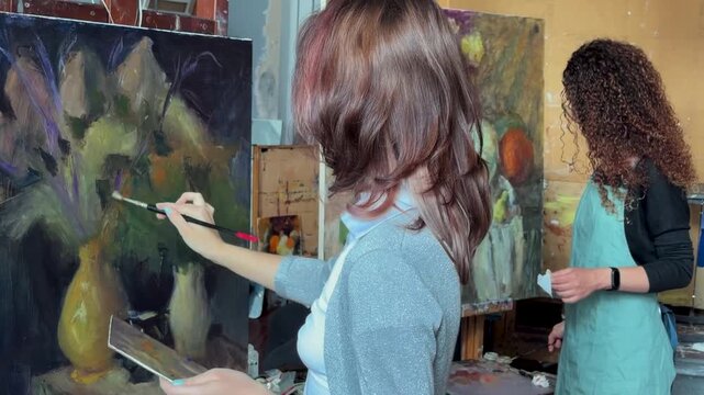 Teenage girl in college painting class, art studio, art workshop. She paints still life on canvas with oil paints. 