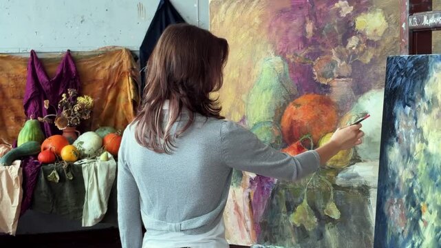 Teenage female artist in college painting class, art studio, art workshop. She paints still life on canvas with oil paints. 