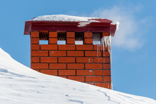 Red brick chimney rises from snowy roof