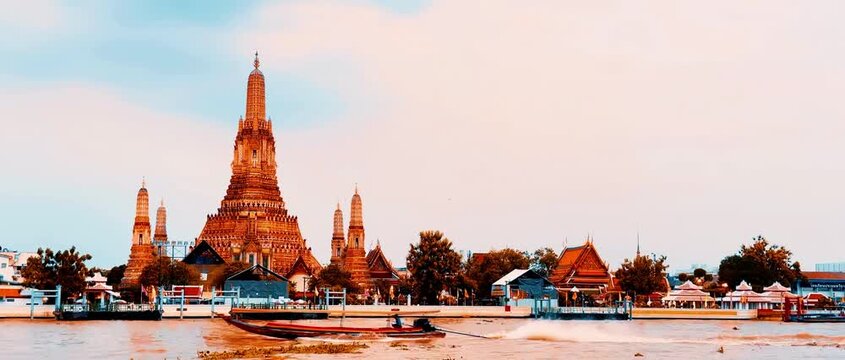 Wat Arun temple standing beside the Chao Phraya River in Bangkok, Thailand, with a traditional long-tail boat crossing the water under a bright cloudy sky, creating a scenic travel view.