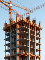 Obraz premium Unfinished concrete tower under construction with cranes and scaffolding against clear blue sky