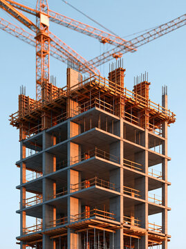 Unfinished concrete tower under construction with cranes and scaffolding against clear blue sky