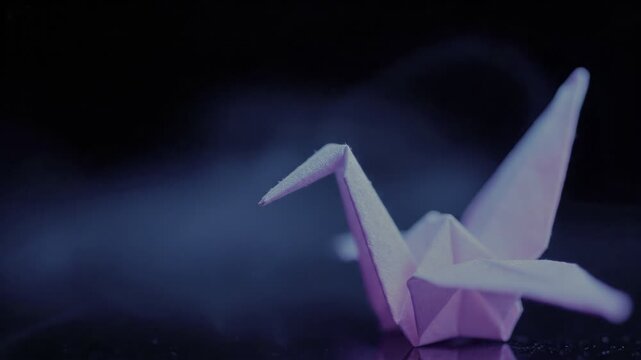 Purple paper origami crane on reflective dark background.