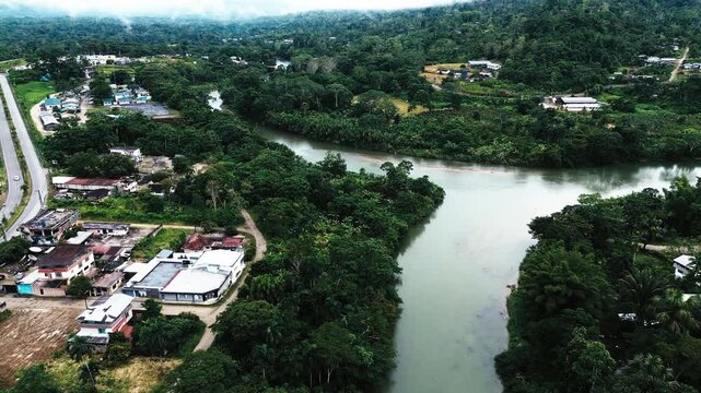 Aerial View of Broad River Beside Tropical Ecuador Town, Green Forest Banks, Urban Buildings, Road Bridge and South American Travel Landscape