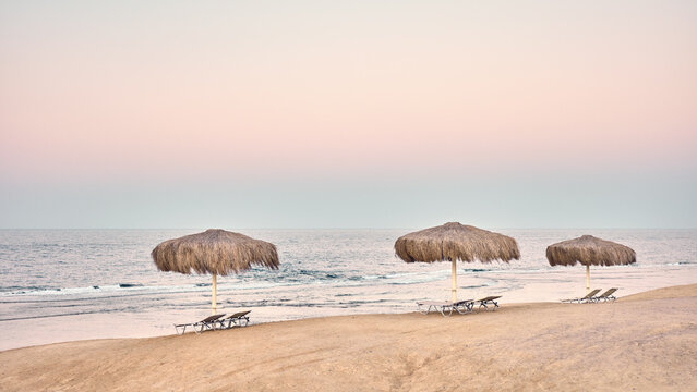 Straw beach umbrellas and lounge chairs on a sandy beach, color toning applied.