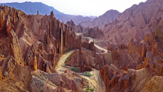 Aerial view of a winding dirt road through rugged red rock canyon ridges in the Red Mountain Stone Forest, Kuqa, Xinjiang, China