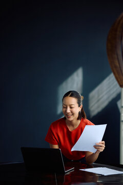 Happy female entrepreneur working on financial reports while using laptop at home.
