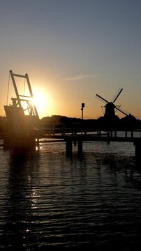 Iconic Dutch windmill and drawbridge silhouetted against a beautiful golden sunset over a tranquil canal in the Netherlands.