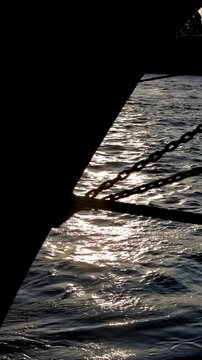 Tranquil vertical video of sun sparkling on river water, framed by a silhouetted pier and chains at sunset.