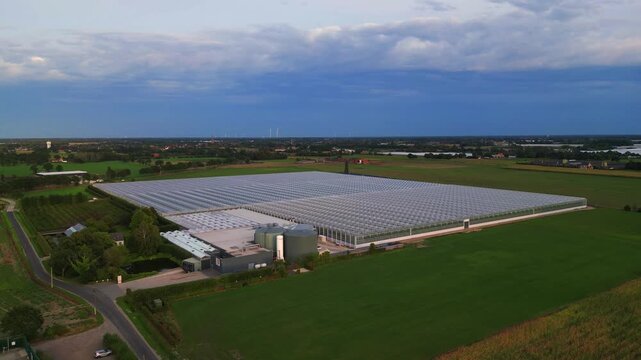 Cinematic aerial view of a massive industrial greenhouse for sustainable food production in a rural landscape.