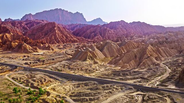 Aerial view of railway tracks running through an arid desert at the foot of red sandstone mountains in the Red Mountain Stone Forest, Kuqa, Xinjiang, China