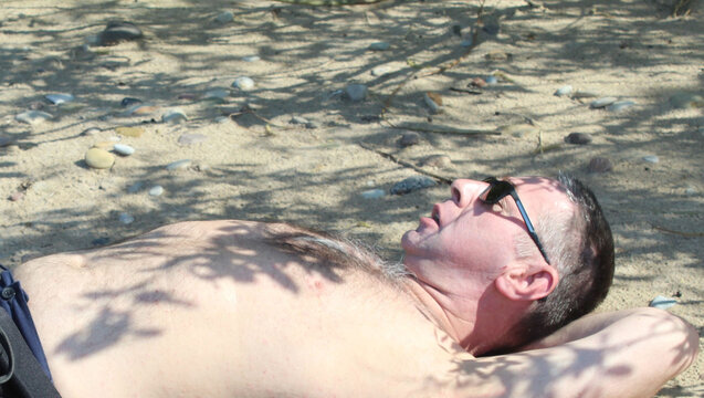 Mature Man Relaxing on Pebble Beach with Backpack in Summer.

