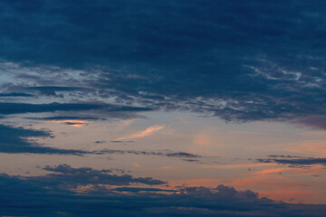 Obraz premium Golden sunlight breaking through dark dramatic storm clouds at sunset, creating a moody atmospheric sky background with glowing sun rays.