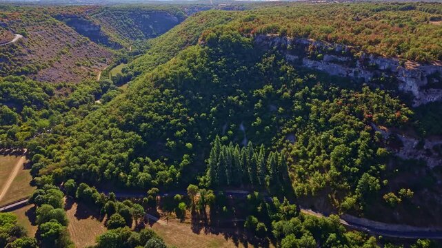Quercy limestone ridge rises above wooded farmland and the D15 near Saint-Sozy, Lot, Occitanie, France, with the Roc des Monges escarpment shaping the valley, drone forward flyover