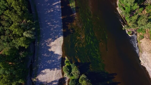 Dordogne River flows beside a broad gravel bank and dense riparian woodland near Saint-Sozy, Lot, Occitanie, France, with shallow rocky sections and riverside vegetation, drone tilt reveal