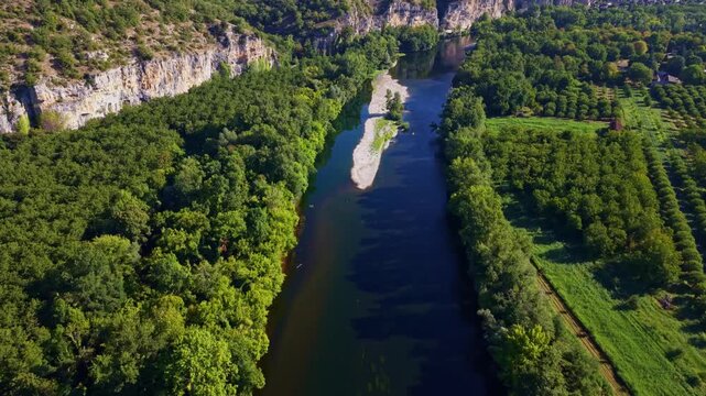 Dordogne River runs beneath the Roc des Monges limestone escarpment near Saint-Sozy, between the Causse de Martel and Causse de Gramat in Lot, Occitanie, France, drone forward flyover tilt up