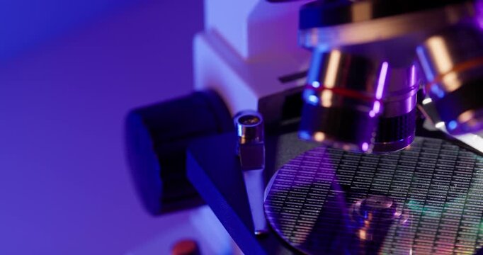 Macro tracking shot of microscope objective lowering onto semiconductor wafer on laboratory bench, factory of microchip.