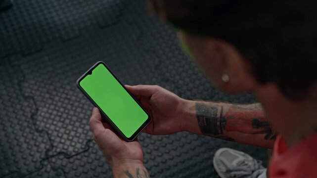 Caucasian young adult man holding smartphone with green screen mockup in gym. Suitable for fitness mobile app presentations, workout tracker demos, and sports technology advertising