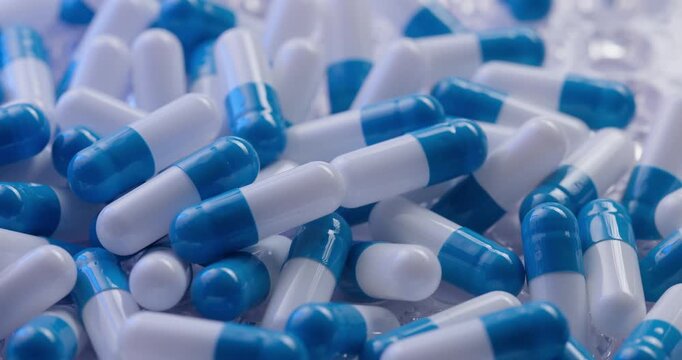 Slow motion blue and white capsules tumbling across plastic blister tray on reflective surface in clinical setting.