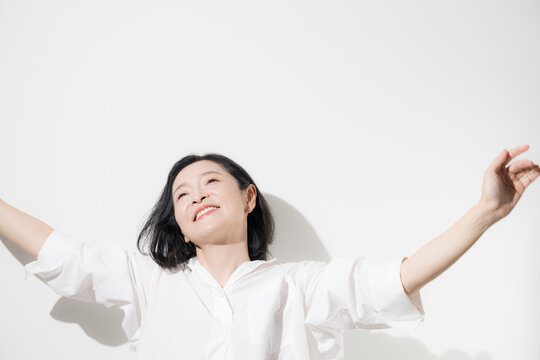 白背景で両手を高く伸ばしてストレッチする50代女性、健康的な生活とリフレッシュを楽しむ爽やかな笑顔のミドル世代　更年期やヘルスケアなどのイメージ	
