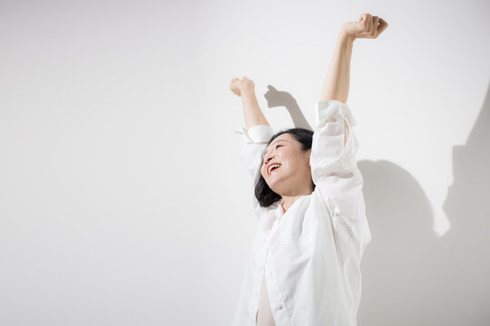 白背景で両手を高く伸ばしてストレッチする50代女性、健康的な生活とリフレッシュを楽しむ爽やかな笑顔のミドル世代　更年期やヘルスケアなどのイメージ	
