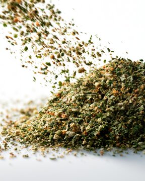 A close-up image of a pile of mixed dried herbs and spices falling against a white background.
