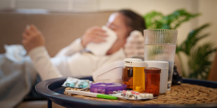 Sick person resting on sofa with medicine and thermometer on table for cold treatment
