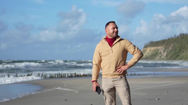 Male traveler stands on a sandy Baltic Sea coast taking a deep breath as a camera pans smoothly from right to left.