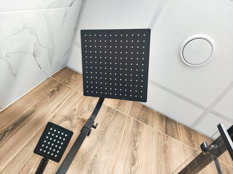 Modern black square rain shower head mounted in bathroom. Minimalist plumbing fixture for luxury walk in shower cabin