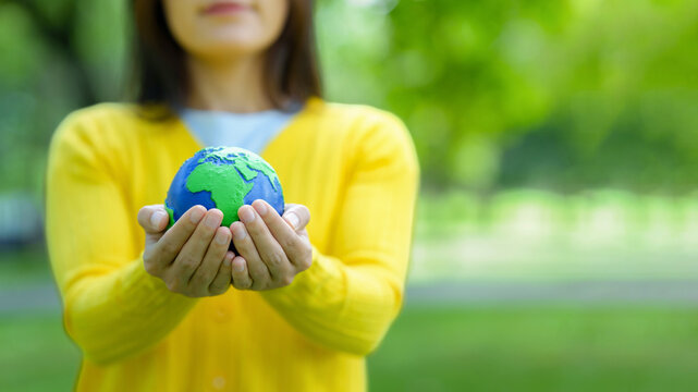 Woman holding earth globe in hands protecting nature environment in park. Ecology concept for sustainability, green future, climate action and global care with natural blurred background. ESG. CSR.