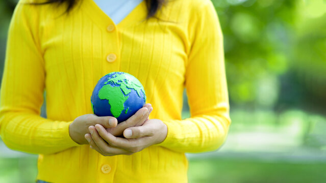 Person holding small earth globe in hands showing environmental conservation concept outdoors. Sustainability, green future, climate action and planet protection in nature park background. ESG. CSR.