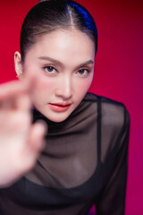 Fototapeta premium A bold woman points directly at the camera with a confident smirk, dramatic foreground blur and sharp gaze against a vivid red backdrop, radiating attitude and defiance.
