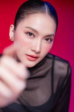 A bold woman points directly at the camera with a confident smirk, dramatic foreground blur and sharp gaze against a vivid red backdrop, radiating attitude and defiance.